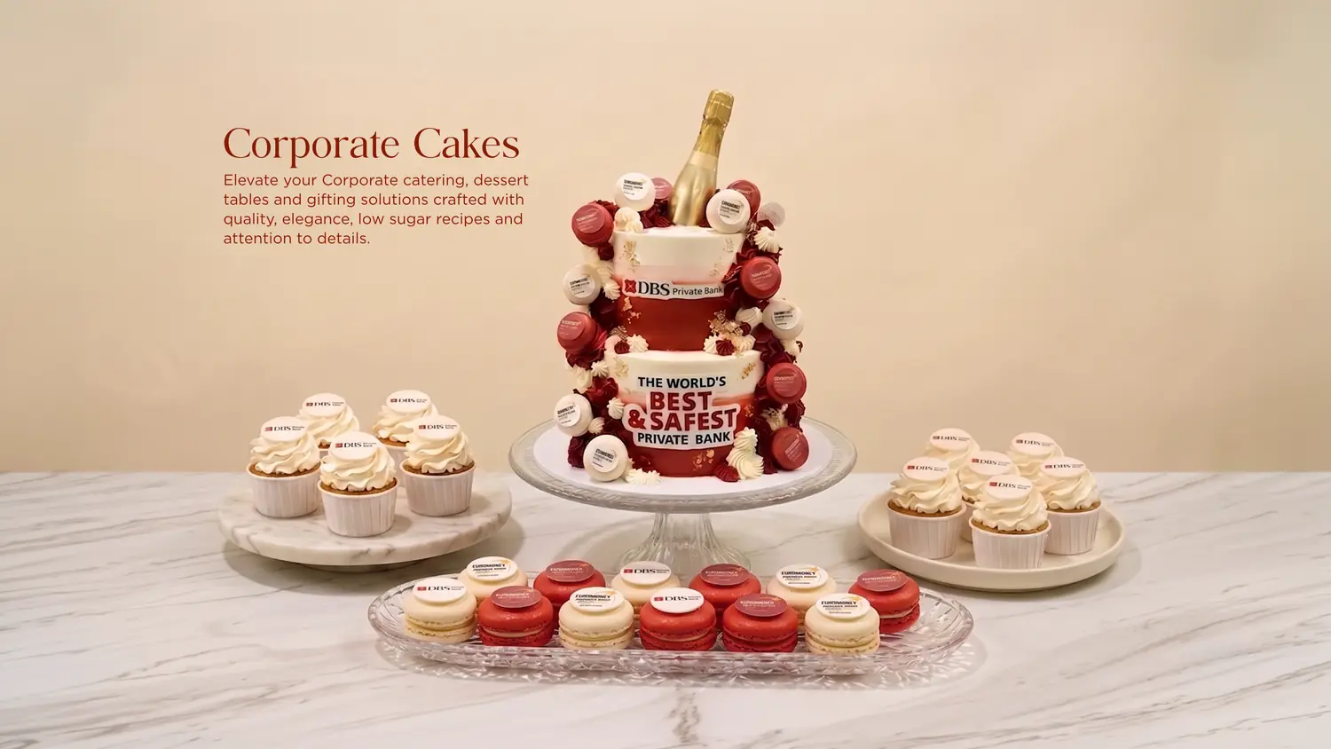 Elegant dessert display for a corporate event: a tall champagne cake adorned with macarons and cupcakes on a marble table.