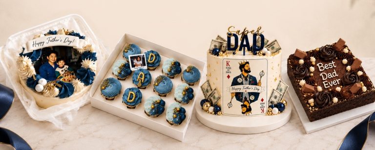 Father's Day dessert spread: photo cake with 'Happy Father's Day' ribbon, box of blue cupcakes spelling DAD, a 'King of Dads' cake with money decorations, and a 'Best Dad Ever' chocolate cake on a marble table.